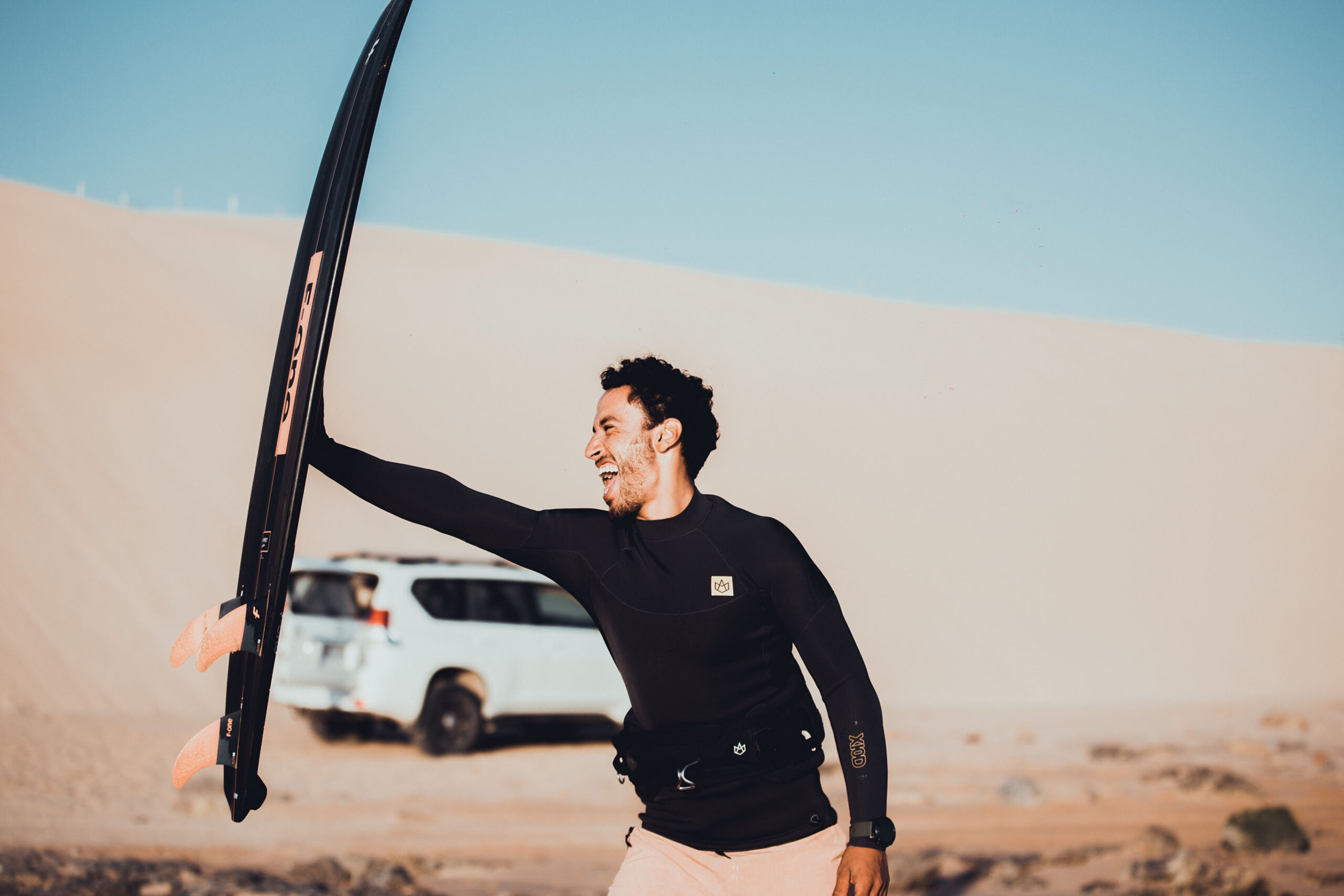 Mogasurf Owner Ismail Adarzane holding F-One Kitesurf board in dunes of Essaouira